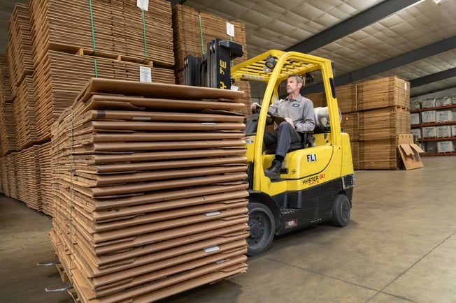 man driving a forklift and moving a stack of gaylord boxes around a warehouse