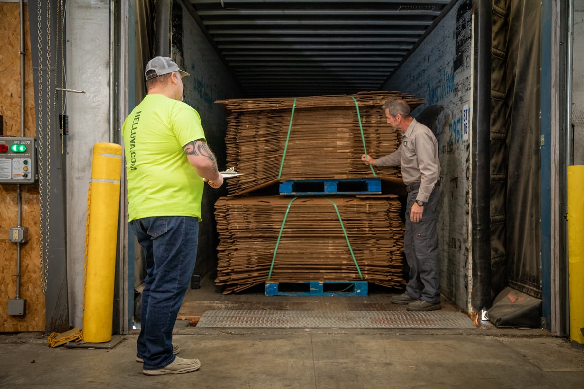 Two men in the back of a trailer checking pallets of flattened Gaylord Boxes
