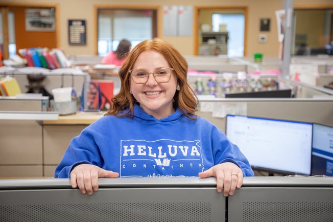 Helluva employee smiling for the camera and looking over an office cubicle divider
